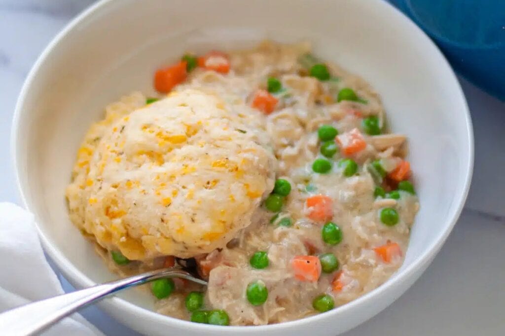 Bowl of chicken pot pie with biscuits and a spoon.