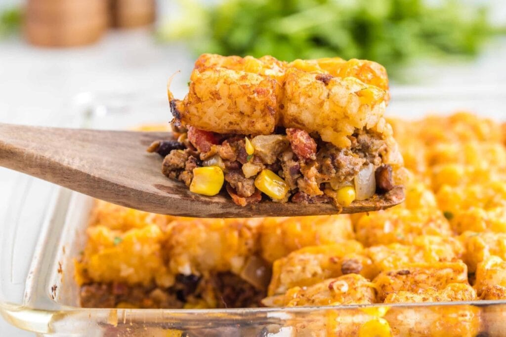 Cowboy casserole in a baking dish, being scooped with a wooden spoon.