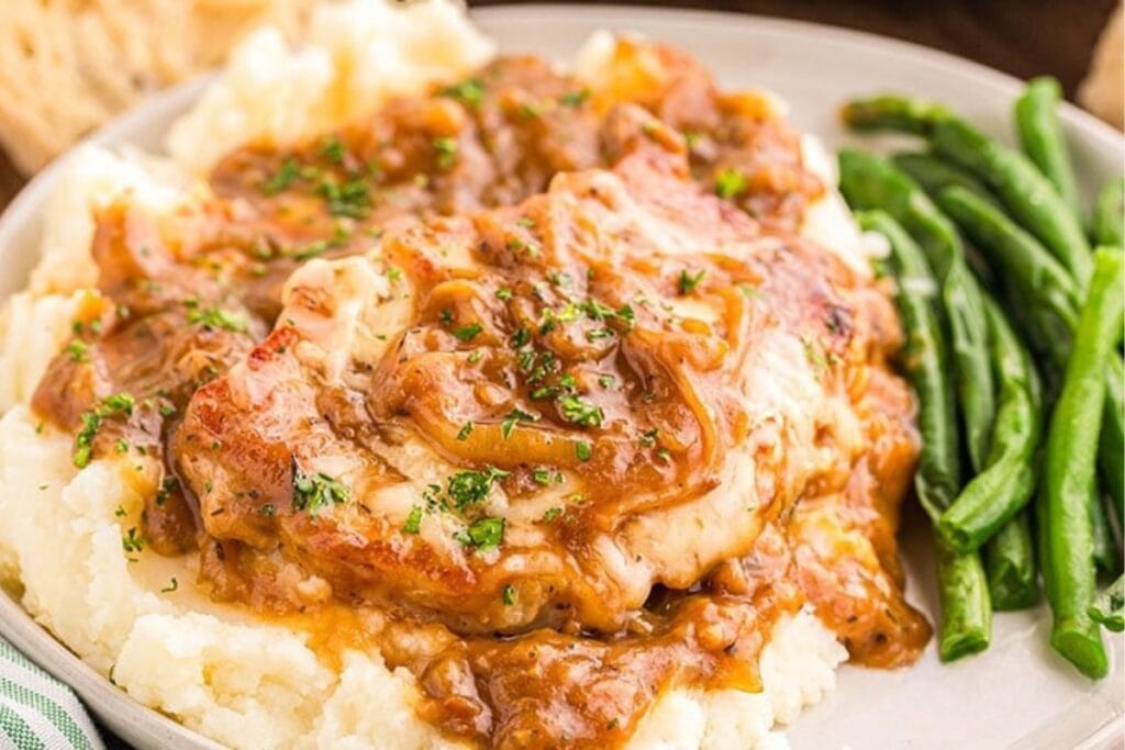 French onion pork chops served on a plate with mashed potatoes and green beans.