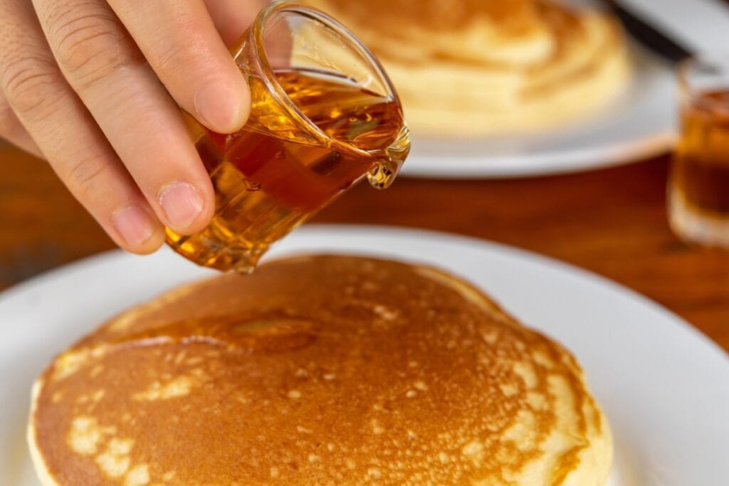 Pouring butter-flavored pancake syrup on a stack of pancakes.