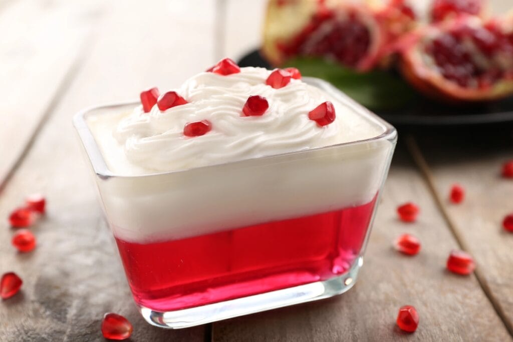 Jello 1-2-3 in a glass dish with cream and pomegranate seeds.