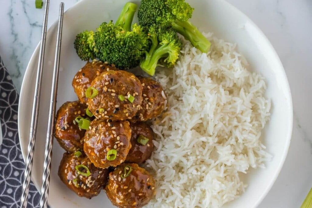 Korean meatballs with sweet spicy BBQ sauce, served with rice and broccoli on a plate.