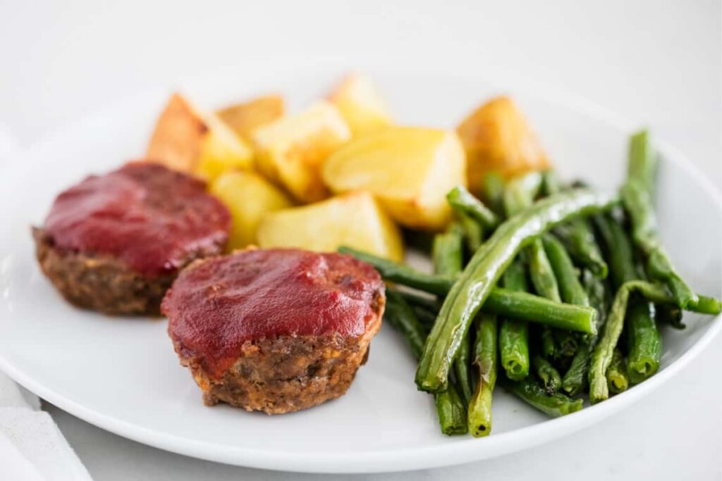 Mini meatloaf muffins on a plate with potatoes and green beans.