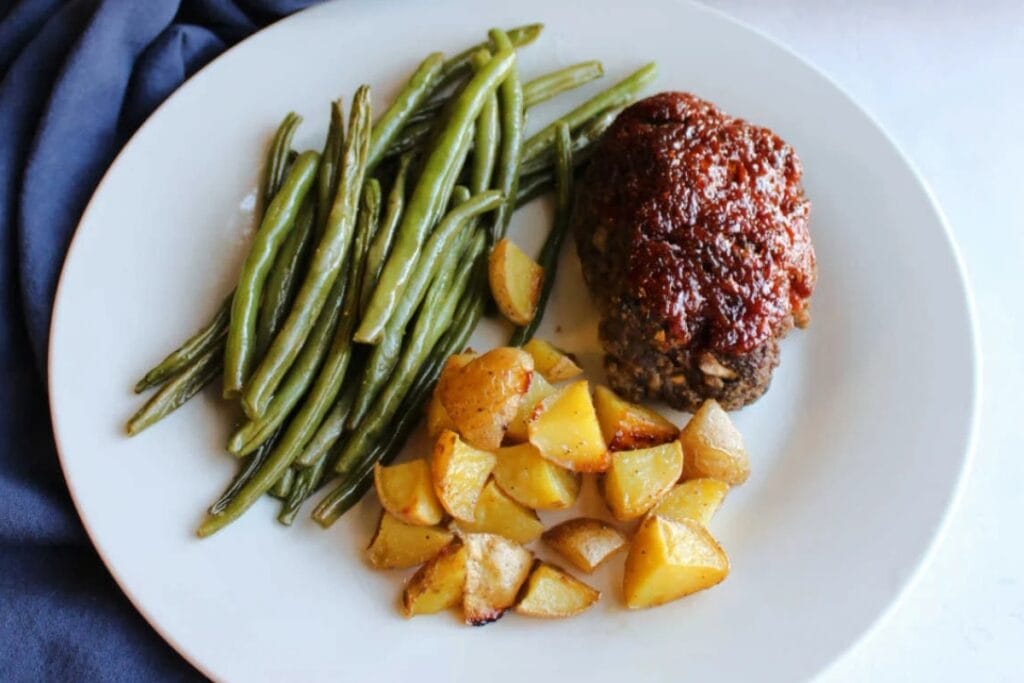 Mini meatloaf with potatoes and green beans on a white plate.