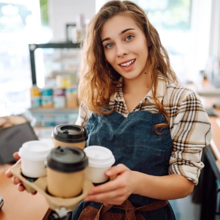 Woman holding a takeout tray with four coffee cups at a café counter