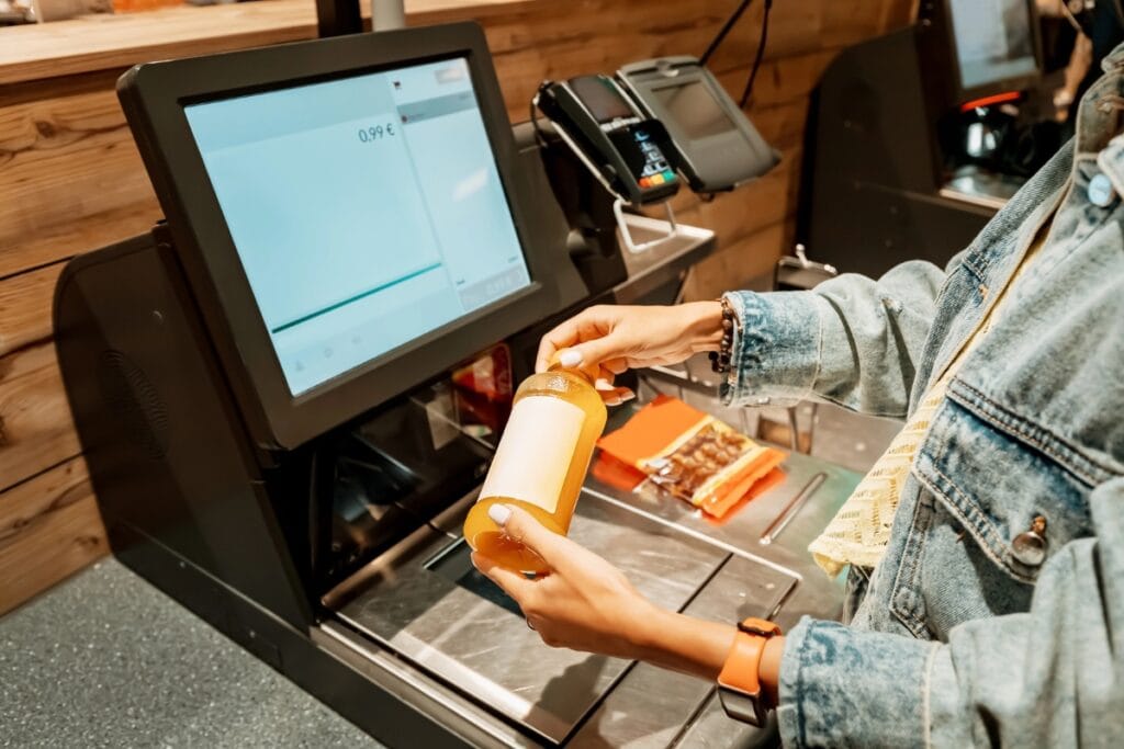 Woman holding a bottle at a self-checkout counter in a store.