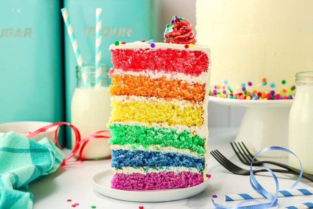 Rainbow layer cake slice on white plate.