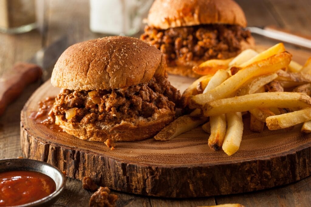 Sloppy joes with fries on a round wooden board.
