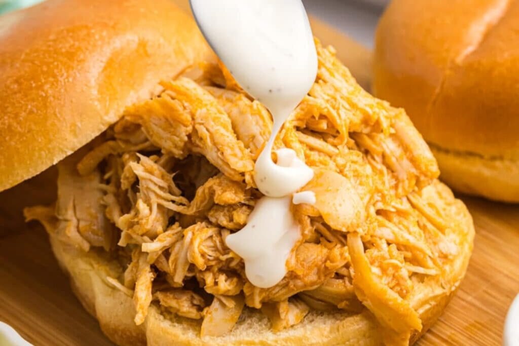 Slow cooker Nashville hot chicken sandwich topped with sauce.