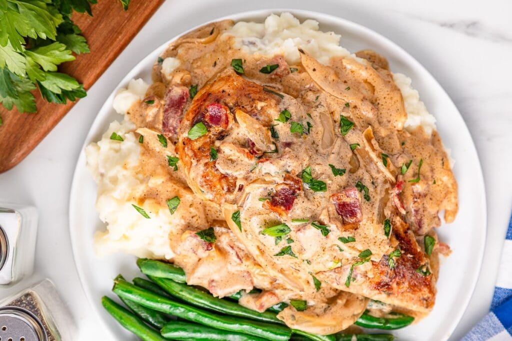 Smothered chicken with gravy on a plate with mashed potatoes and green beans.