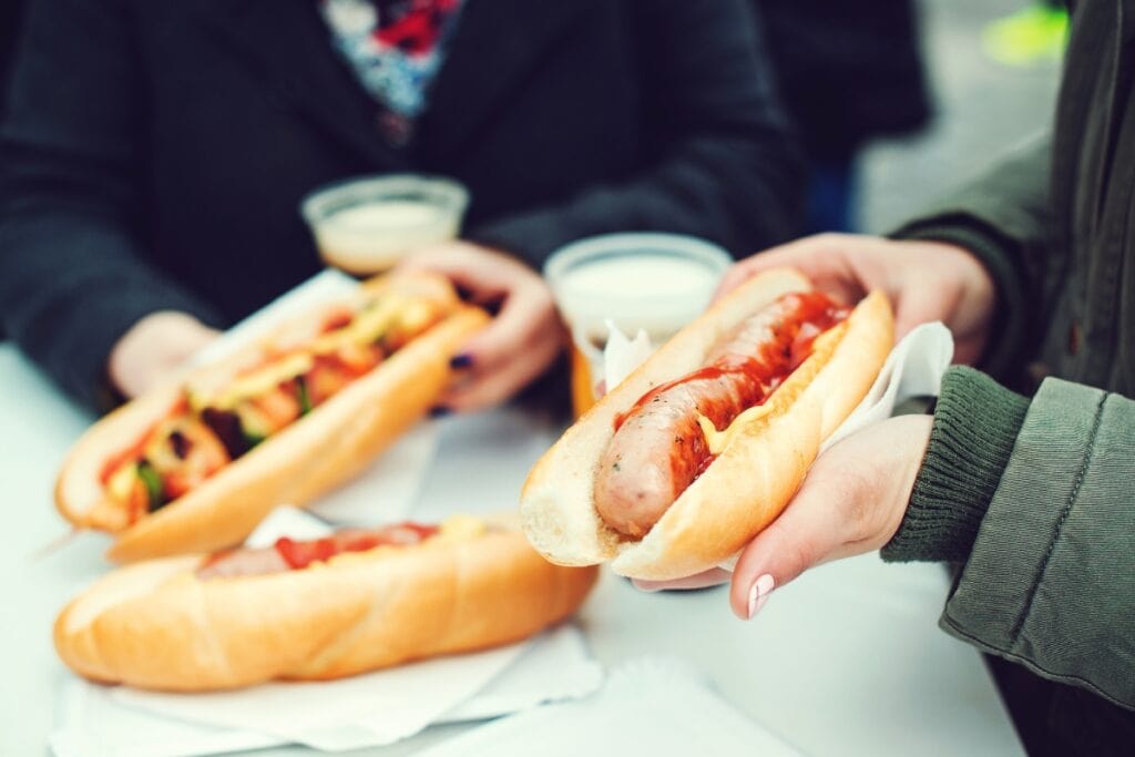 Hotdogs and sandwiches with drinks on a concession stand table.