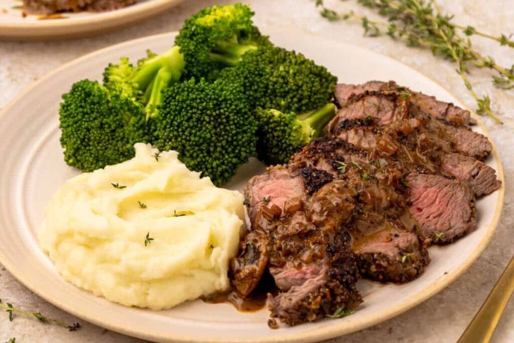 Steak topped with mushroom sauce, served with broccoli and mashed potatoes on a plate.