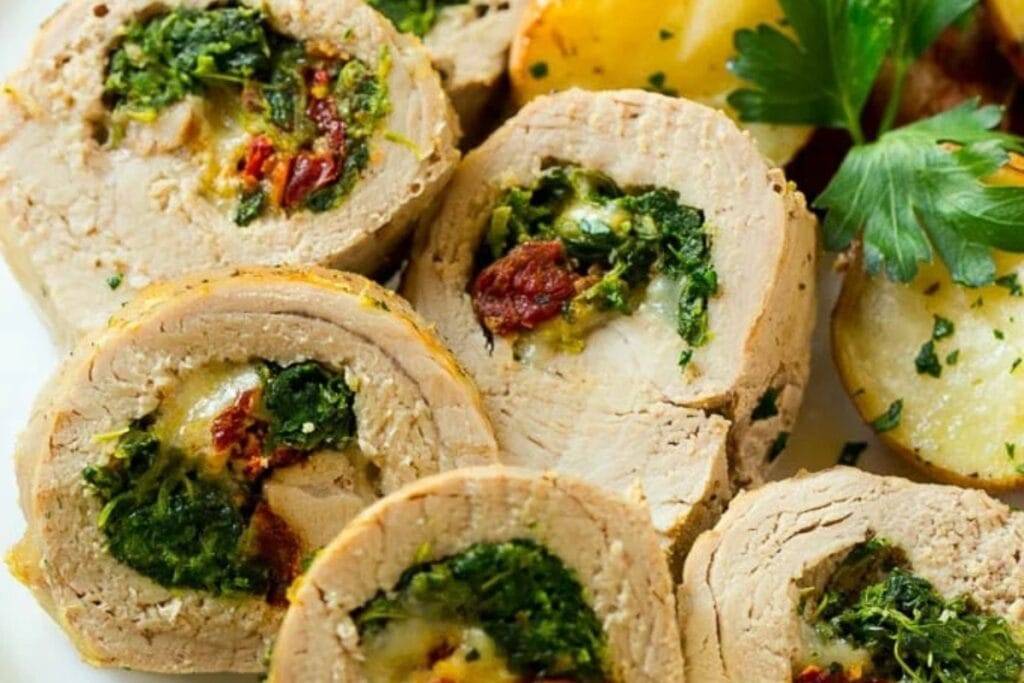 Stuffed pork tenderloin with roasted potatoes and parsley on a plate.