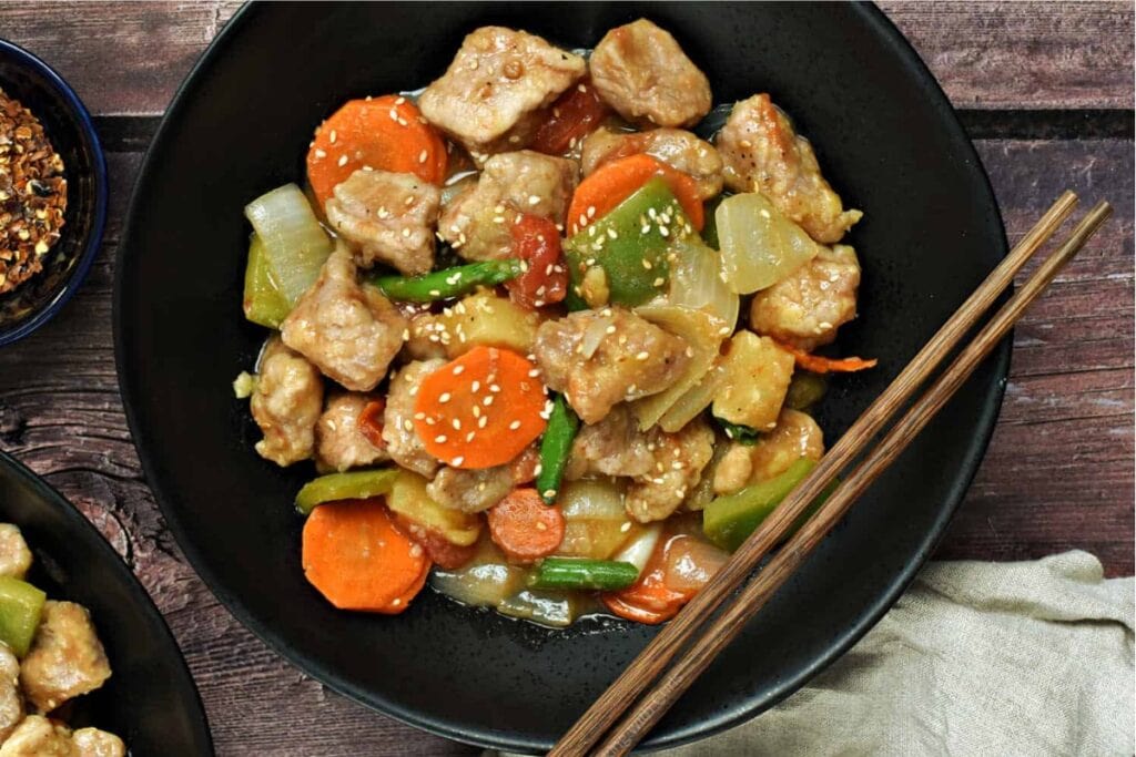 Sweet and sour pork on a black plate with chopsticks on the side.