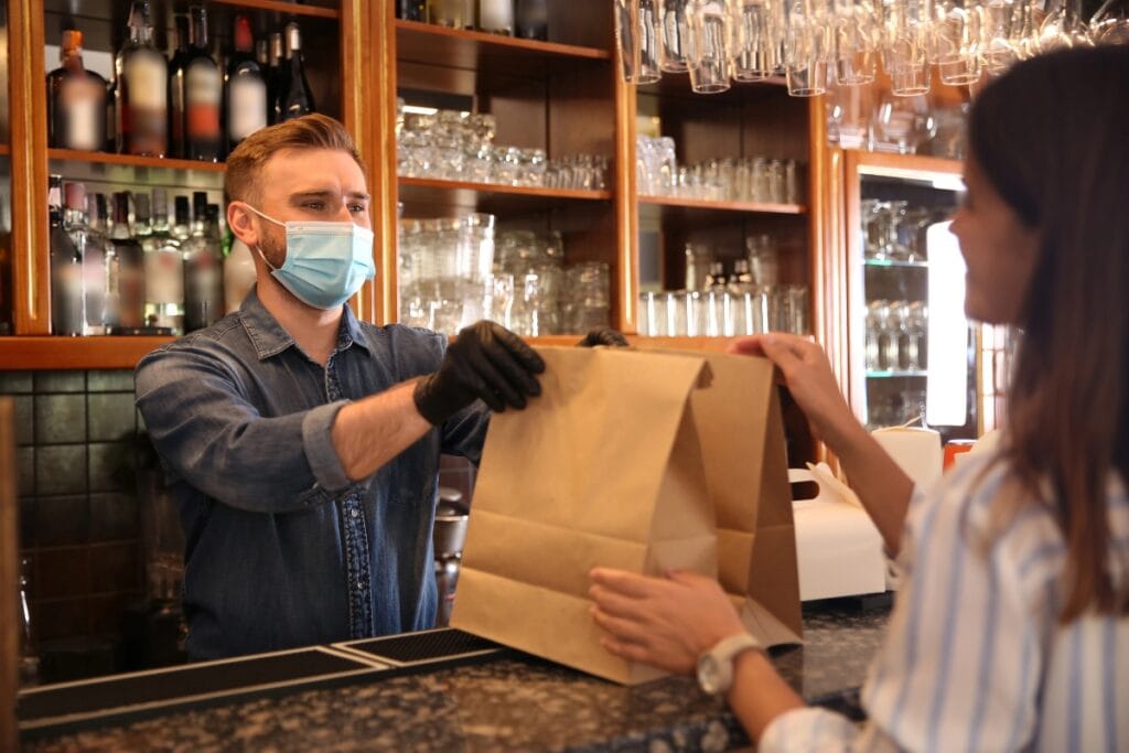 Man handing two paper takeout bags to a woman customer.