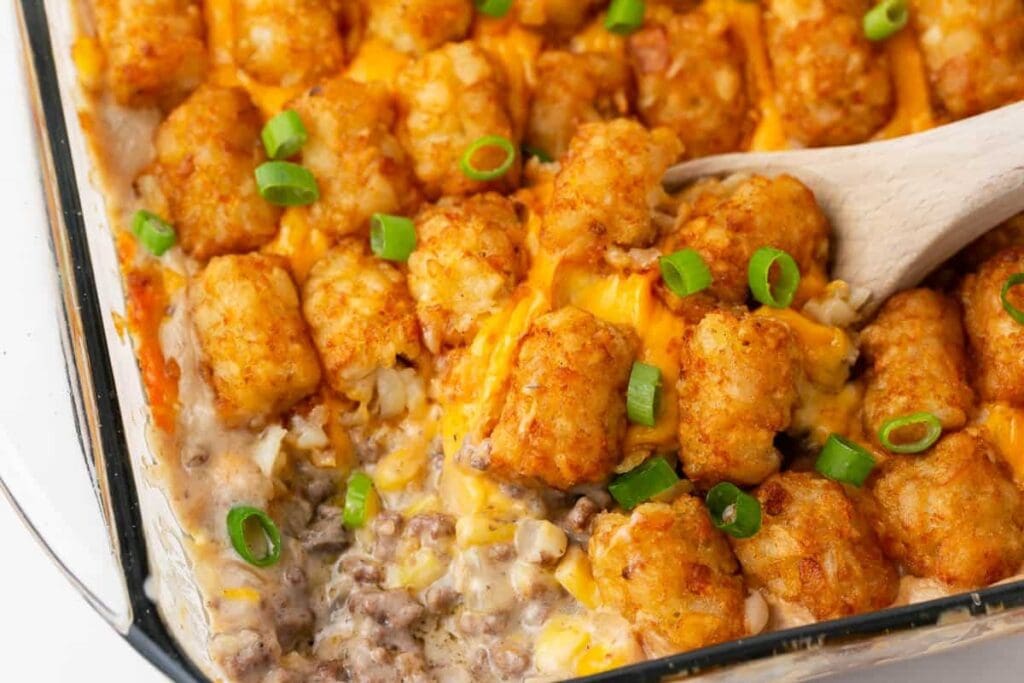 Tater tot casserole in a baking dish with a wooden spoon.