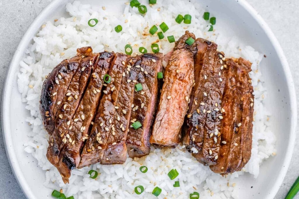 Teriyaki steak served on top of rice on a plate.
