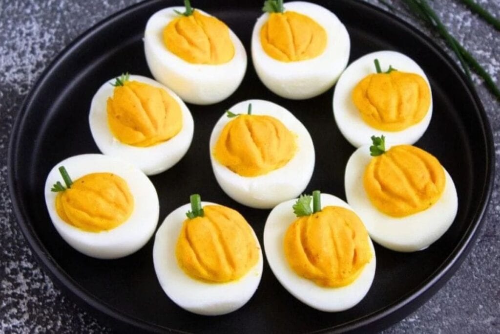 deviled eggs that look like little pumpkin on black plate and dark background
