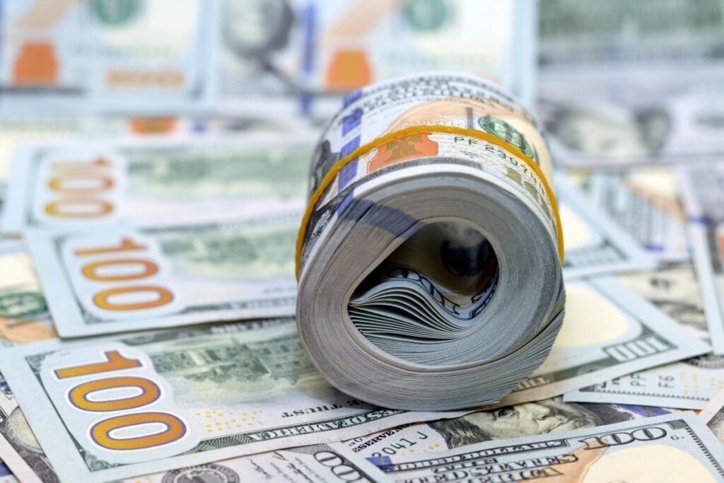 Bundle of rolled dollar bills on top of $100 banknotes.