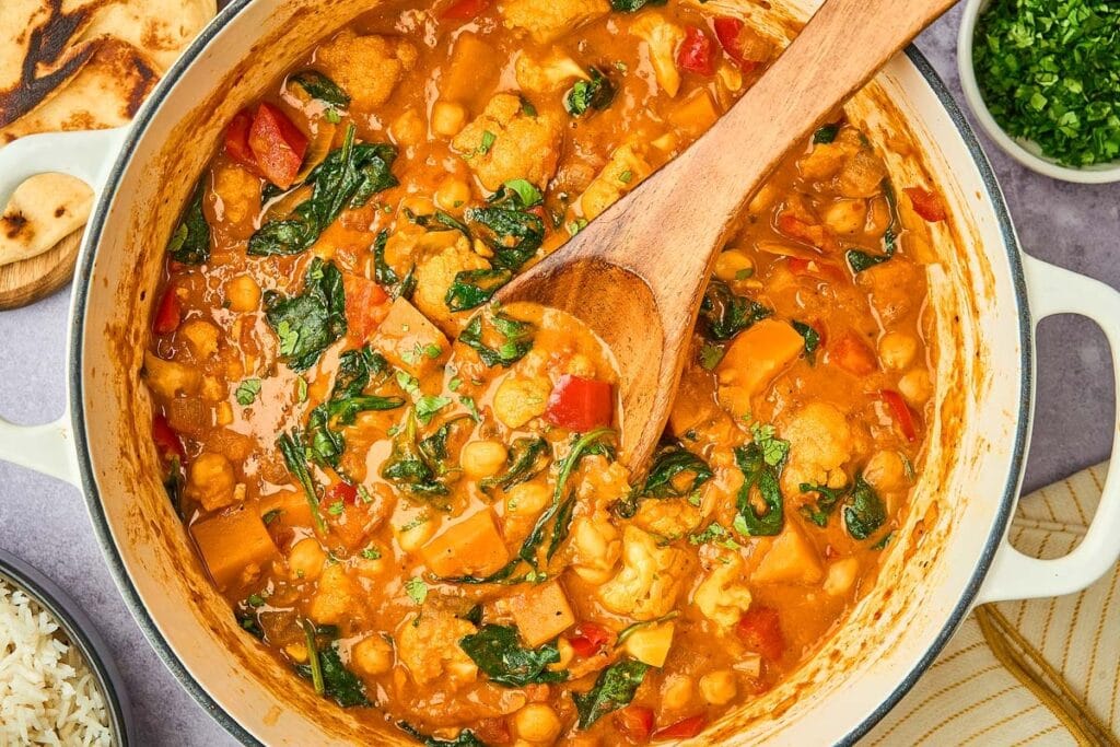 Vegetable curry in pot with wooden ladle.