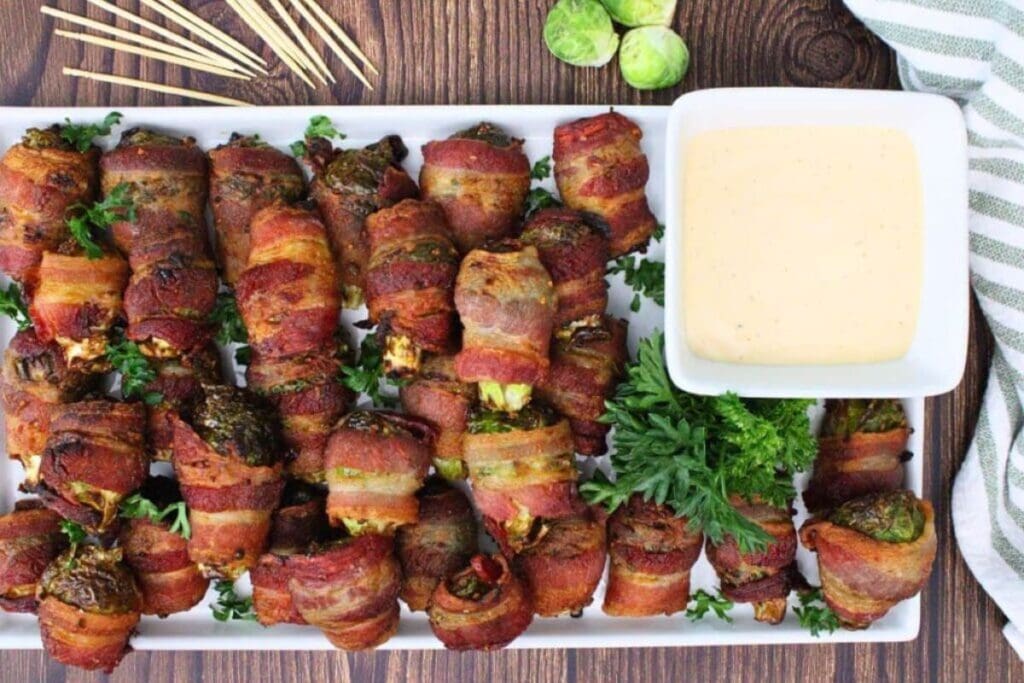 Bacon-wrapped Brussels sprouts on a white platter with dipping sauce.