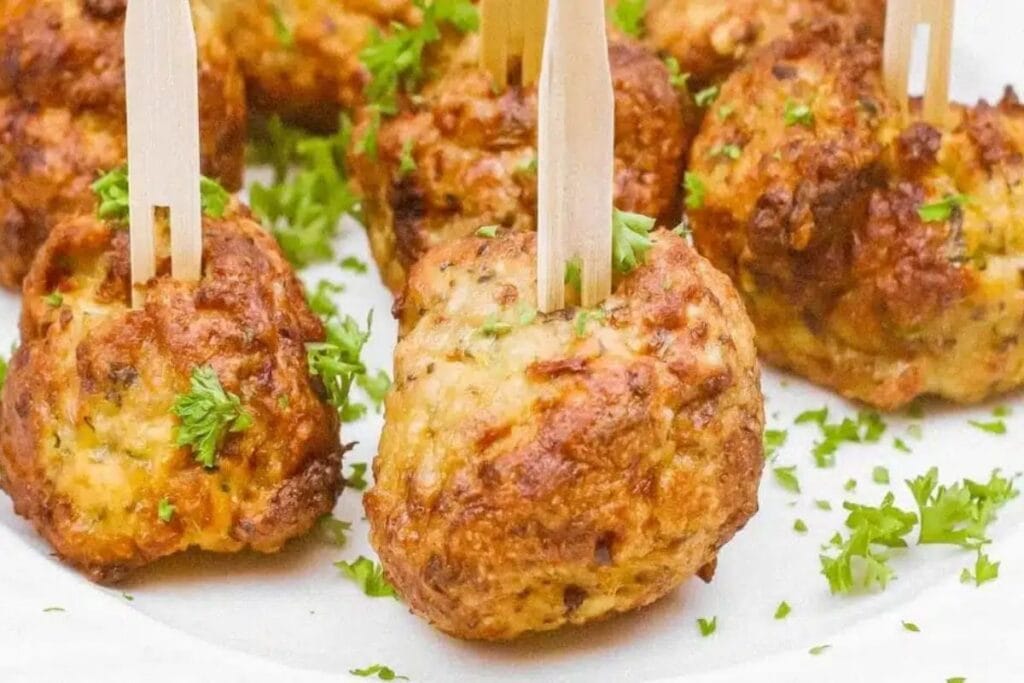 Chicken meatballs on a white plate with parsley and wooden skewers.
