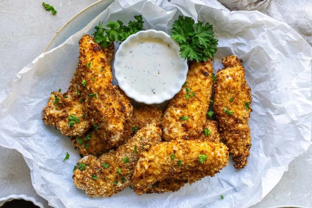 Crispy air fryer chicken tenders with dipping sauce and parsley garnish.