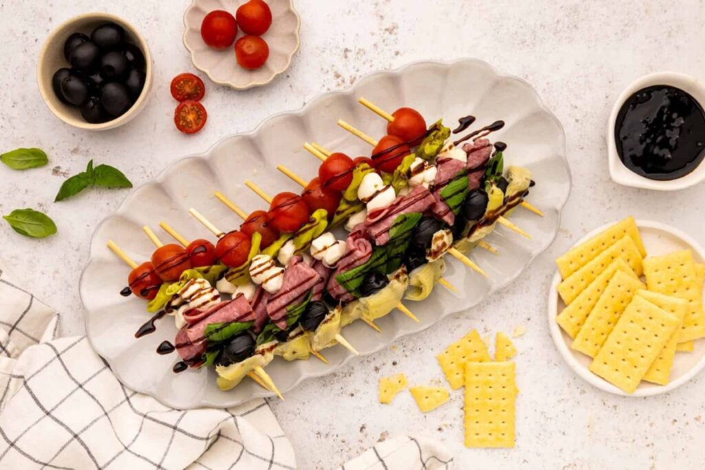 Overhead shot of antipasto skewers on a platter with crackers and olives.