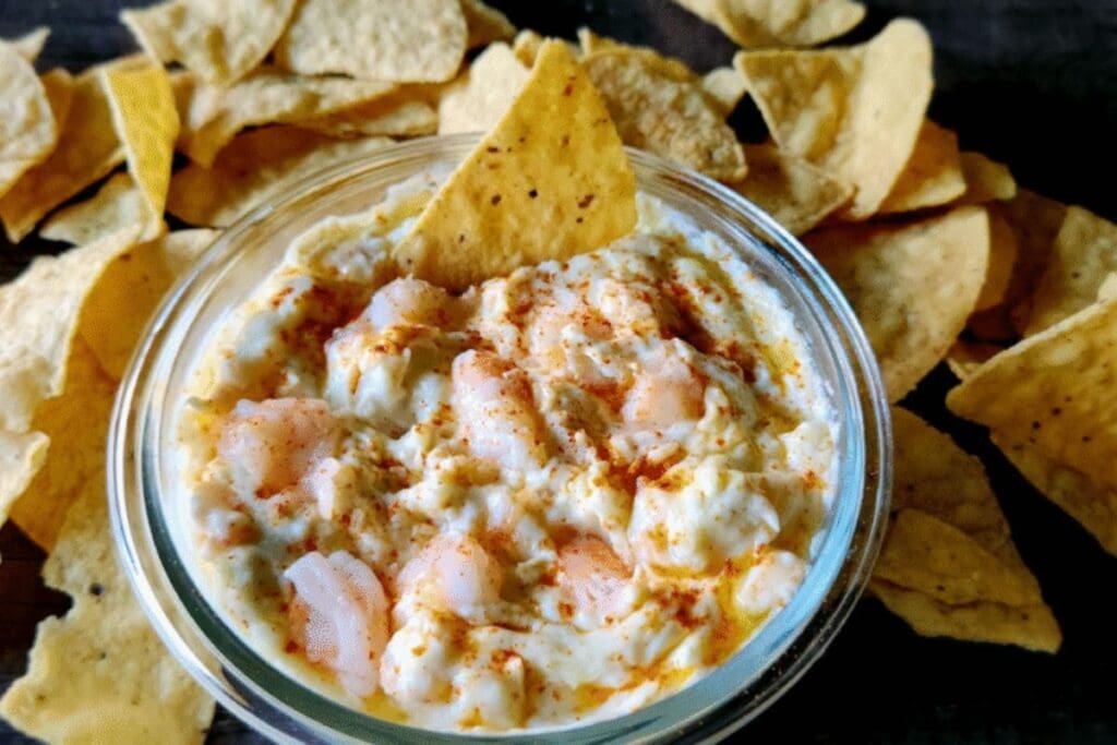 Artichoke shrimp and cheese party dip in a glass bowl with tortilla chips.