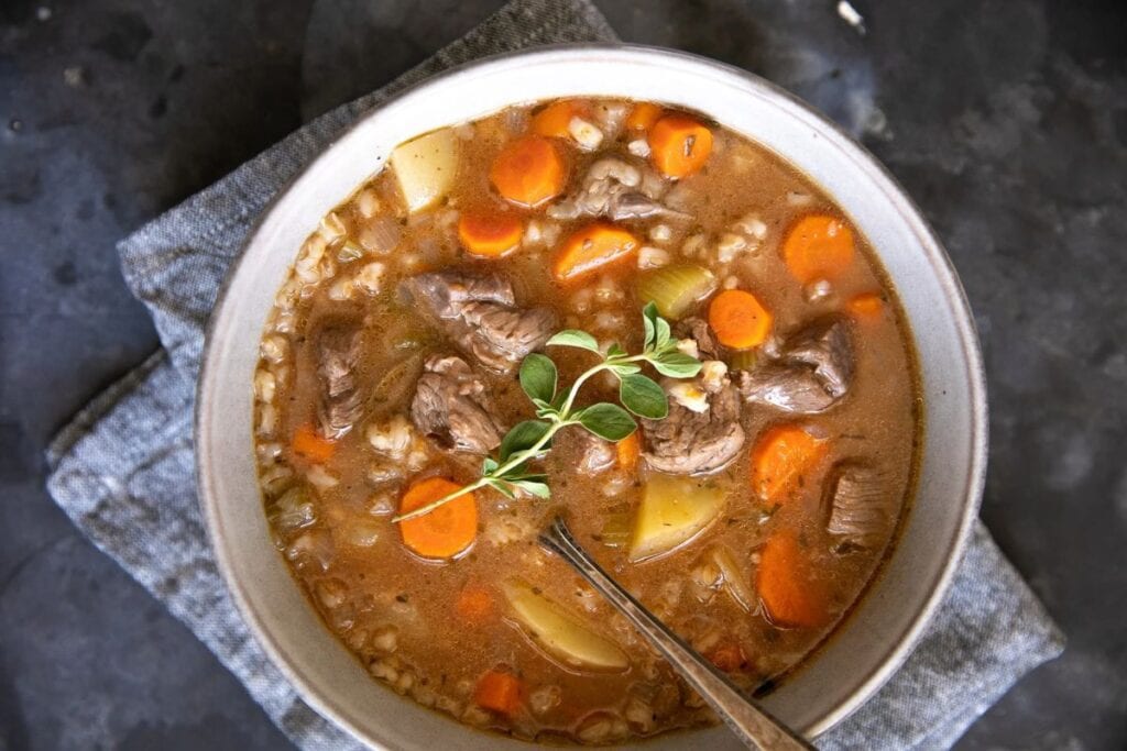 Bowl of beef barley soup with carrots and potatoes, garnished with thyme.