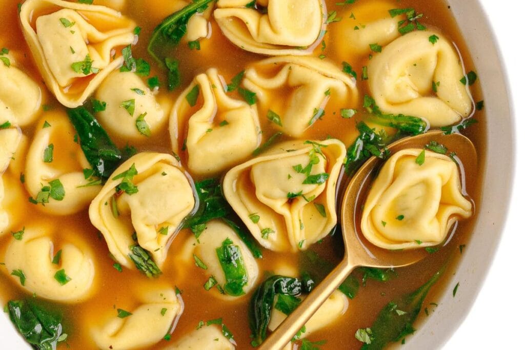 Close-up of beef tortellini soup with spinach and parsley.