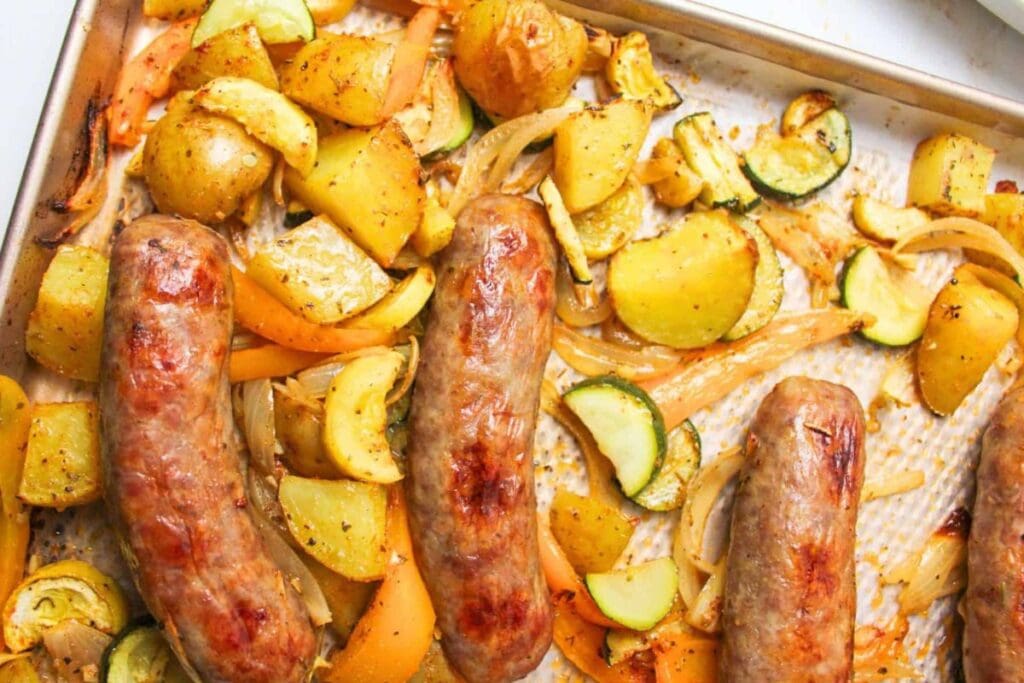 Sheet pan dinner with bratwurst, potatoes, zucchini, onions, and bell peppers.