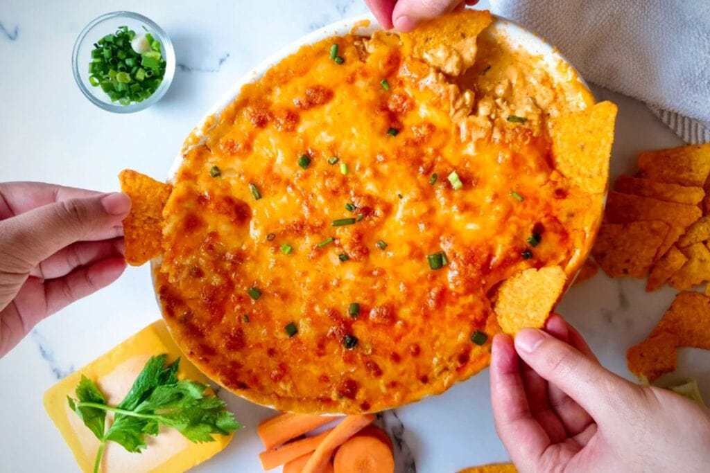 Overhead view of buffalo chicken dip with tortilla chips, celery, and carrots.