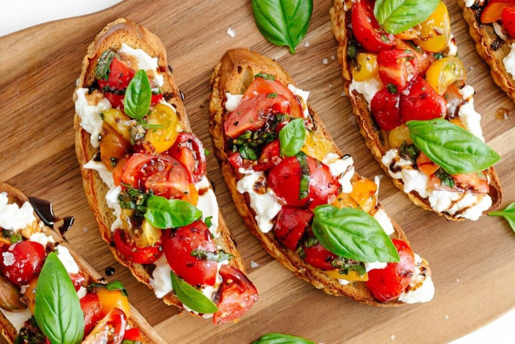 Bruschetta with burrata cheese, tomatoes, basil, and balsamic glaze on a wooden board.