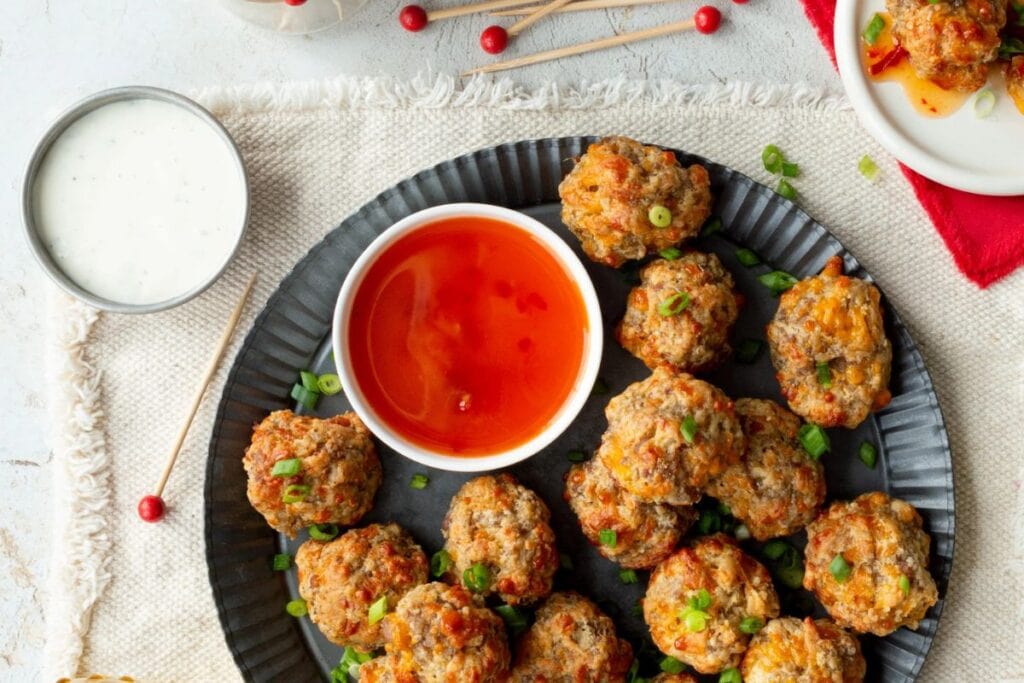 Sausage balls with cheddar cheese on a plate with dipping sauces.