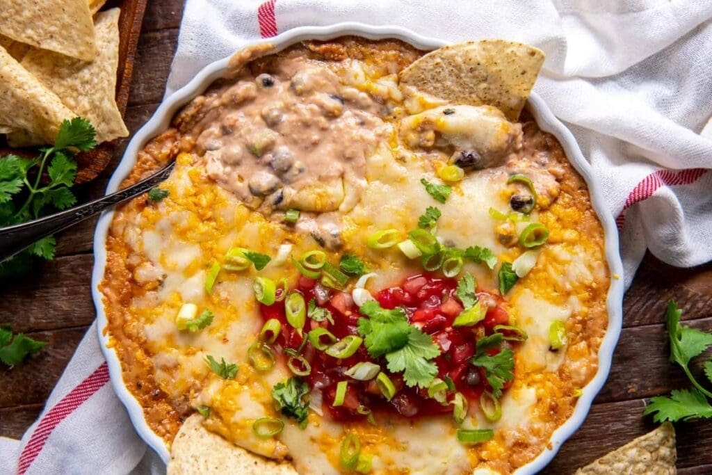 Layered cheesy bean dip with salsa, green onions, cilantro, and tortilla chips.