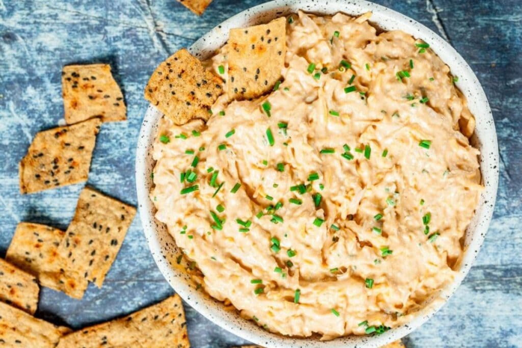 Cheesy chicken dip in a bowl, garnished with chives, served with crackers.