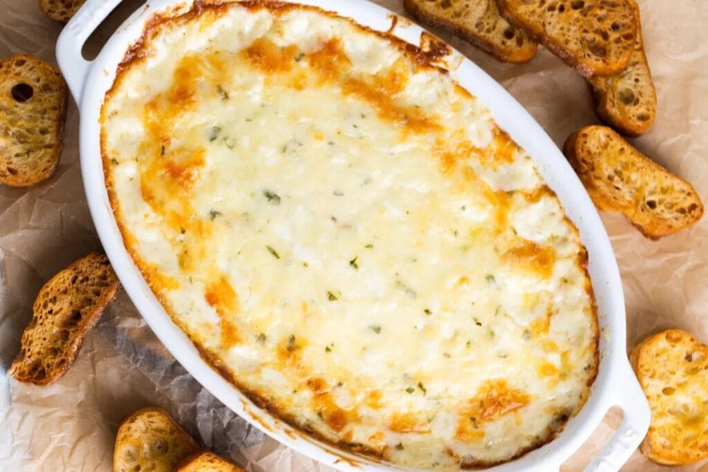 Cheesy garlic bread dip in a white dish with toasted bread slices.