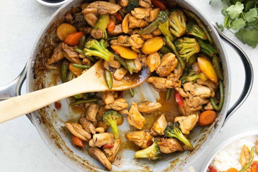 Chicken stir-fry with broccoli, carrots, and green beans in a skillet.