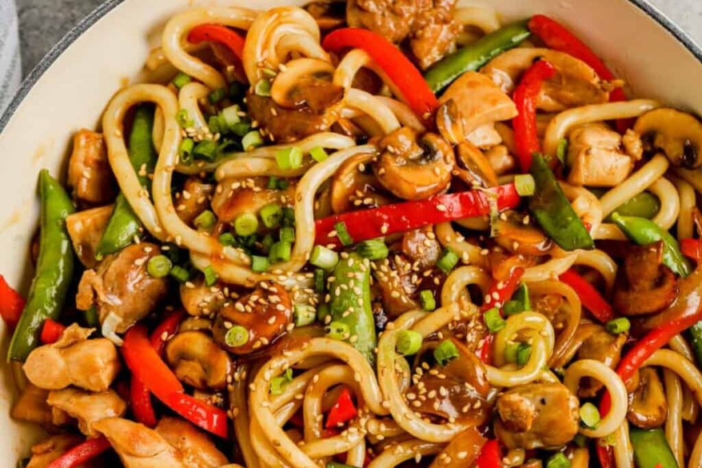 Chicken udon stir fry with mushrooms, red peppers, and snow peas.