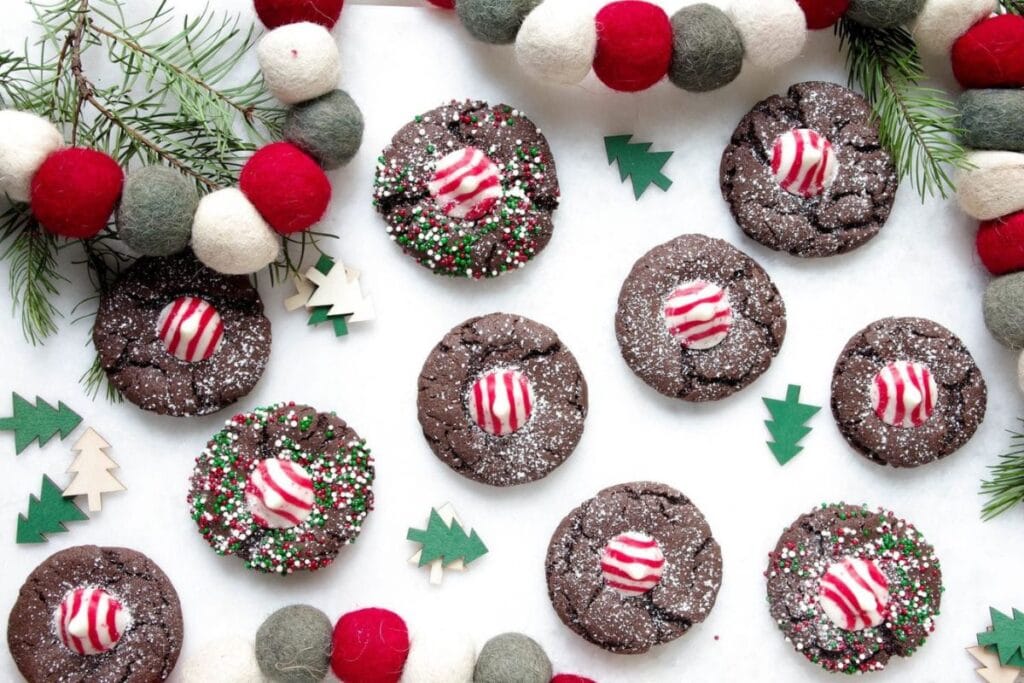 Overhead shot of chocolate cookies with peppermint candies and sprinkles, decorated with Christmas garland and trees.