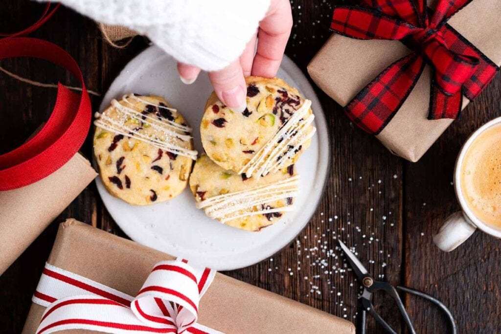 A hand reaching for a cookie on a plate surrounded by gifts and coffee.