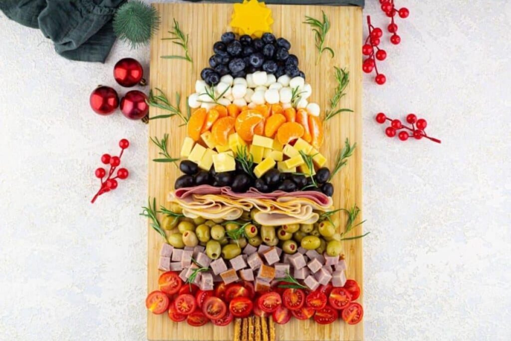 Christmas tree-shaped charcuterie board with fruits, cheese, meats, and olives.