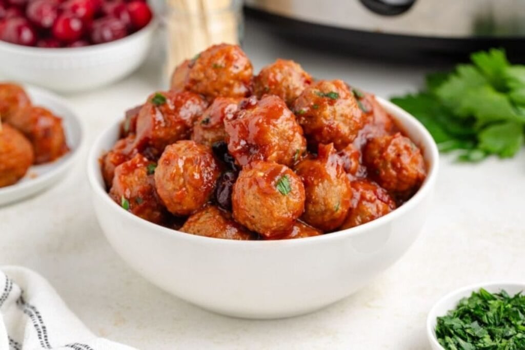 Meatballs with cranberry sauce in a white bowl, garnished with parsley.