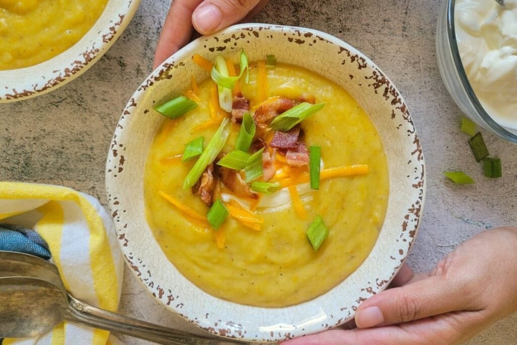Hands holding a bowl of baked potato soup with bacon, cheese, and green onions.