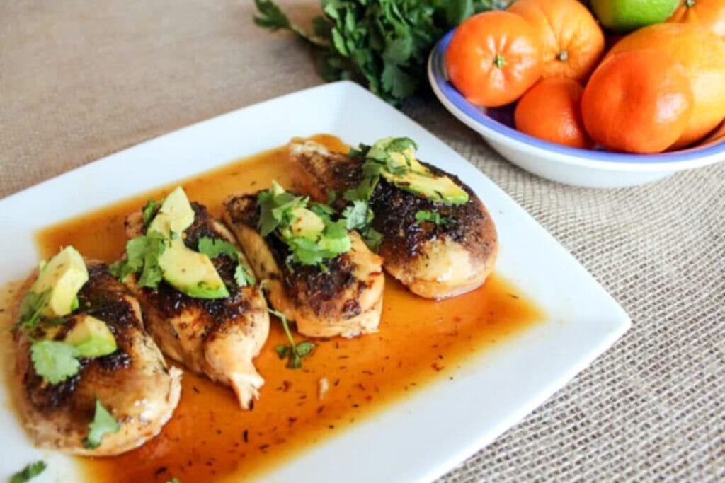 Jerk chicken breasts with sauce, topped with avocado and cilantro on a white plate.
