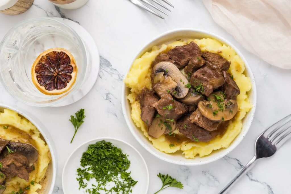Overhead shot of beef tips and gravy over mashed potatoes with mushrooms.