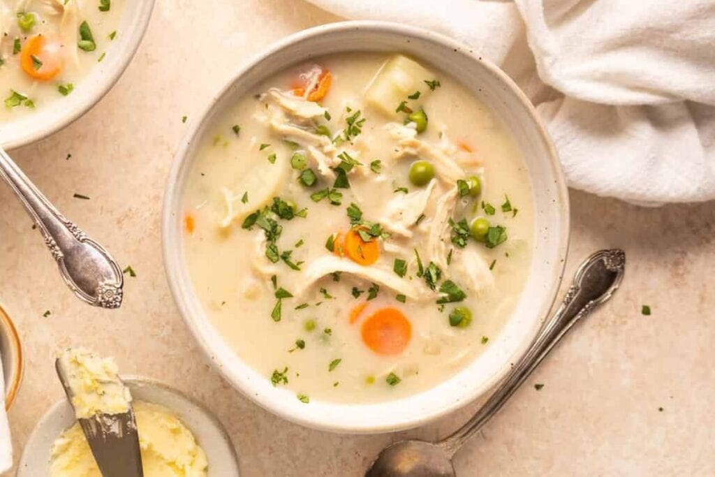 Chicken pot pie soup in a bowl with carrots, peas, potatoes, and parsley.