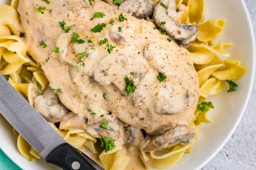 Chicken breast with mushroom sauce over egg noodles, garnished with parsley.