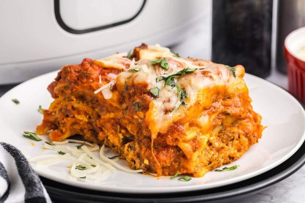 Slice of lasagna with melted cheese and parsley on a white plate.